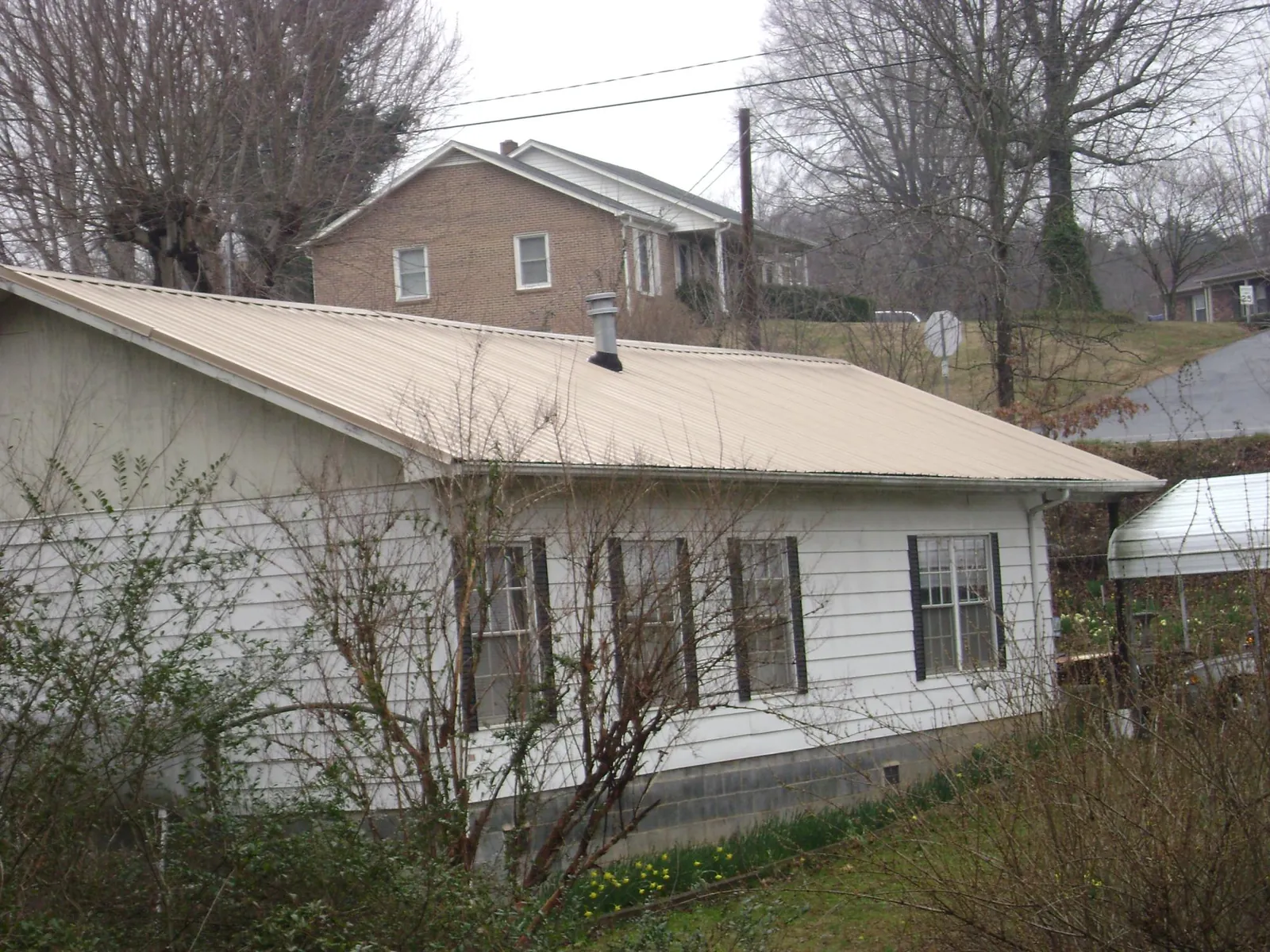 Tan metal roof on a white sided house set into a hillside — Commercial Roofing by Roofing Brothers in Hickory